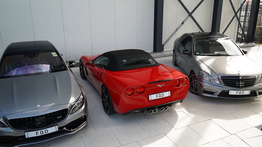 Drie occasions naast elkaar voor de loods van FQD: een grijze Mercedes-AMG, een rode Corvette cabriolet en een Mercedes E-klasse.